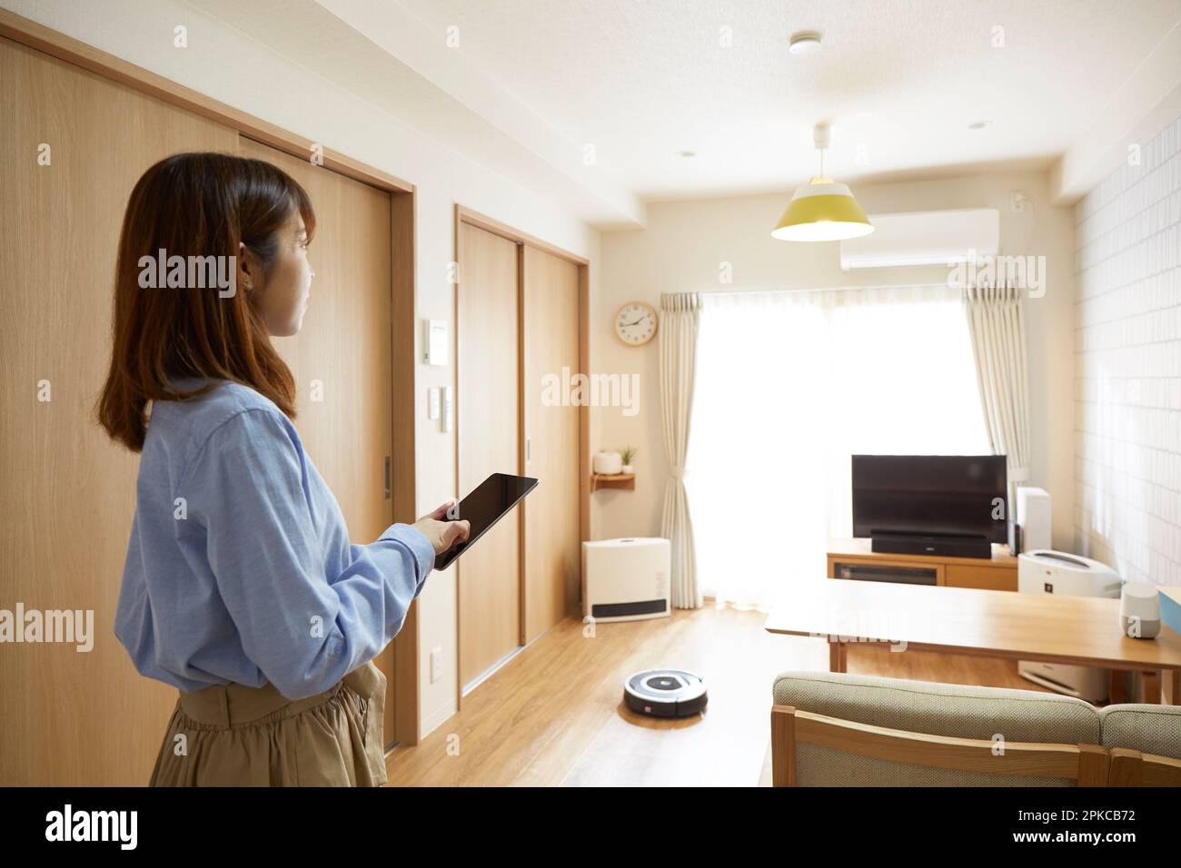 Donna che utilizza robot e tablet per la pulizia in salotto Foto Stock