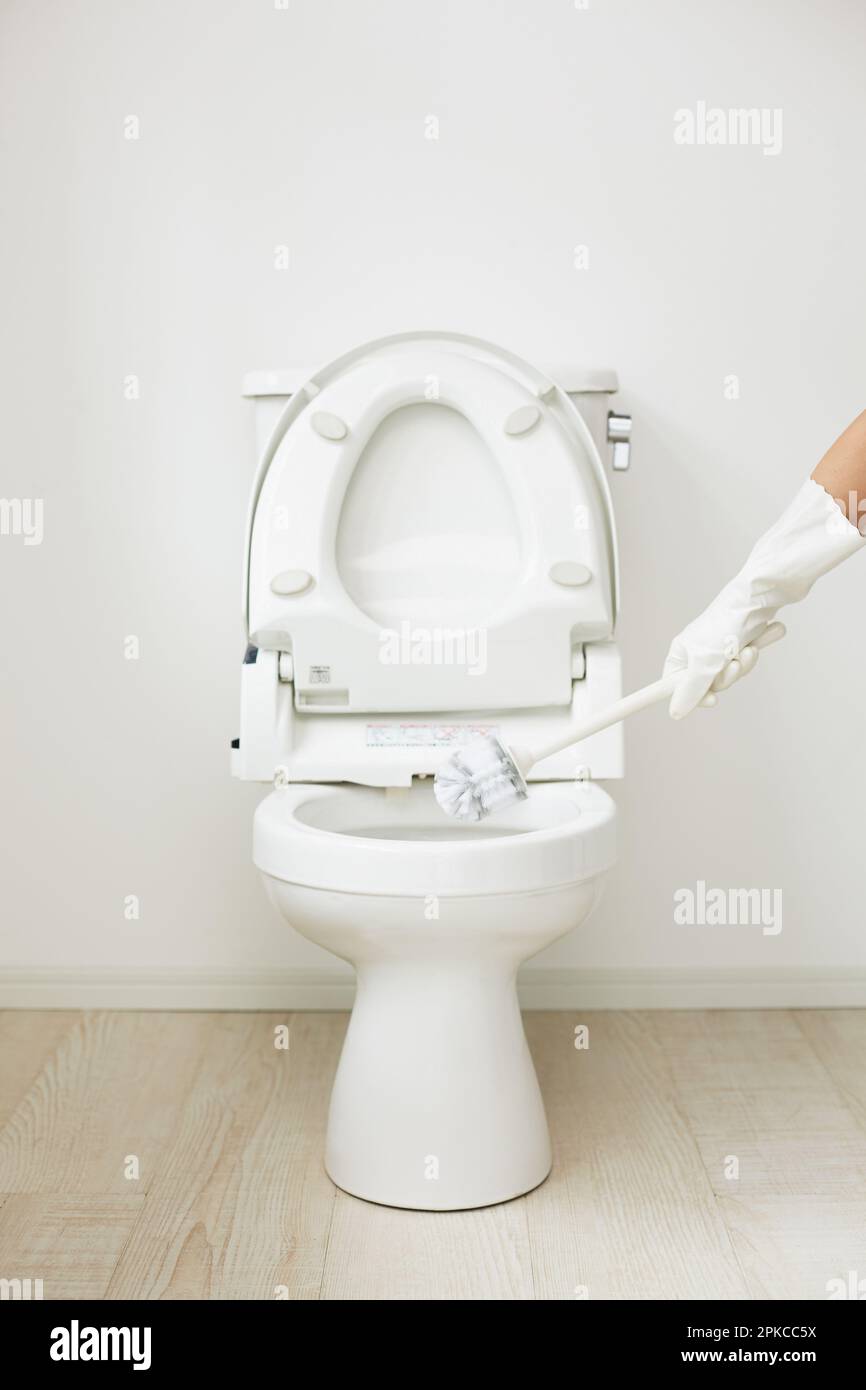 Spazzola per la pulizia della toilette e della mano nello spazio tra il pavimento bianco e la parete Foto Stock