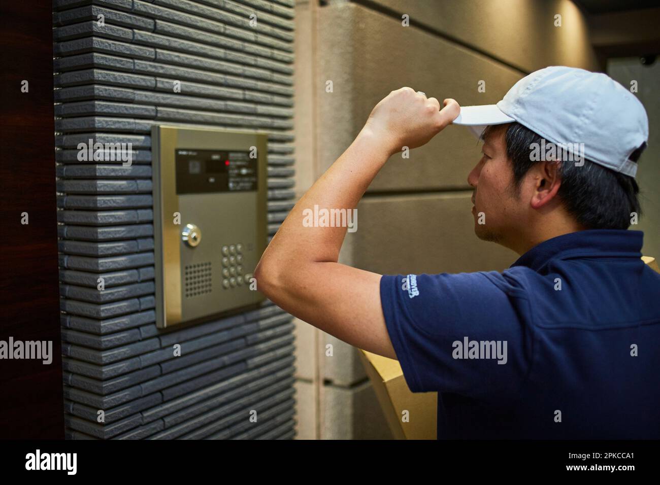 Uomo in abiti da lavoro in piedi di fronte al citofono di un appartamento Foto Stock