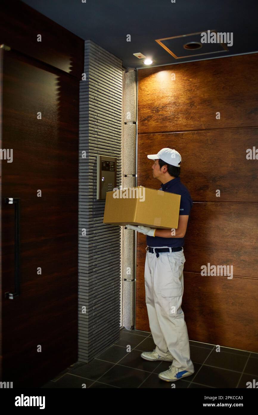 Uomo in abiti da lavoro che spinge il citofono di un appartamento Foto Stock