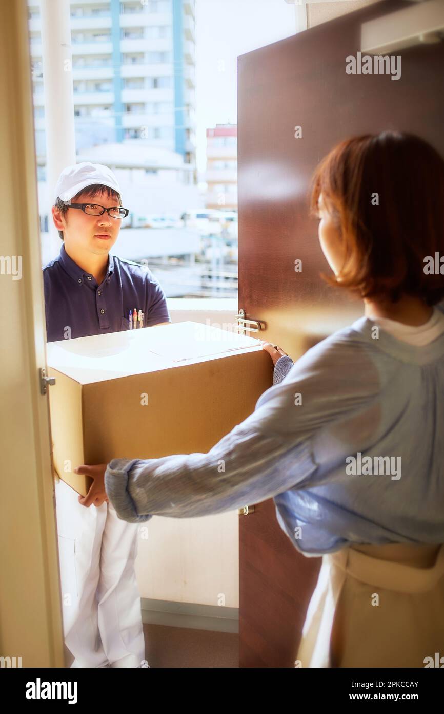 Uomo in abiti da lavoro che consegna scatole di cartone all'ingresso e donna che li riceve Foto Stock