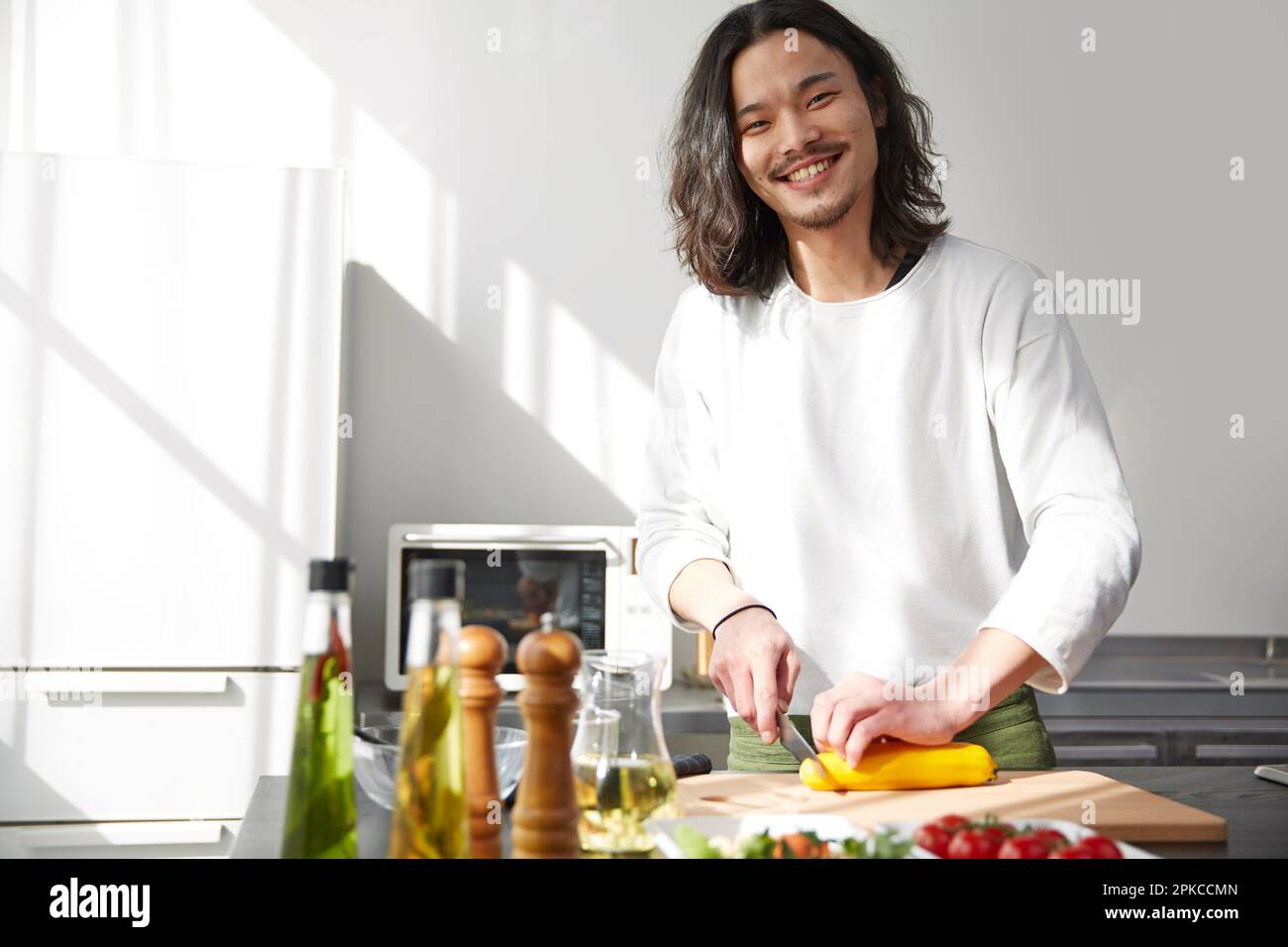 Uomo sorridente che taglia le verdure in cucina Foto Stock