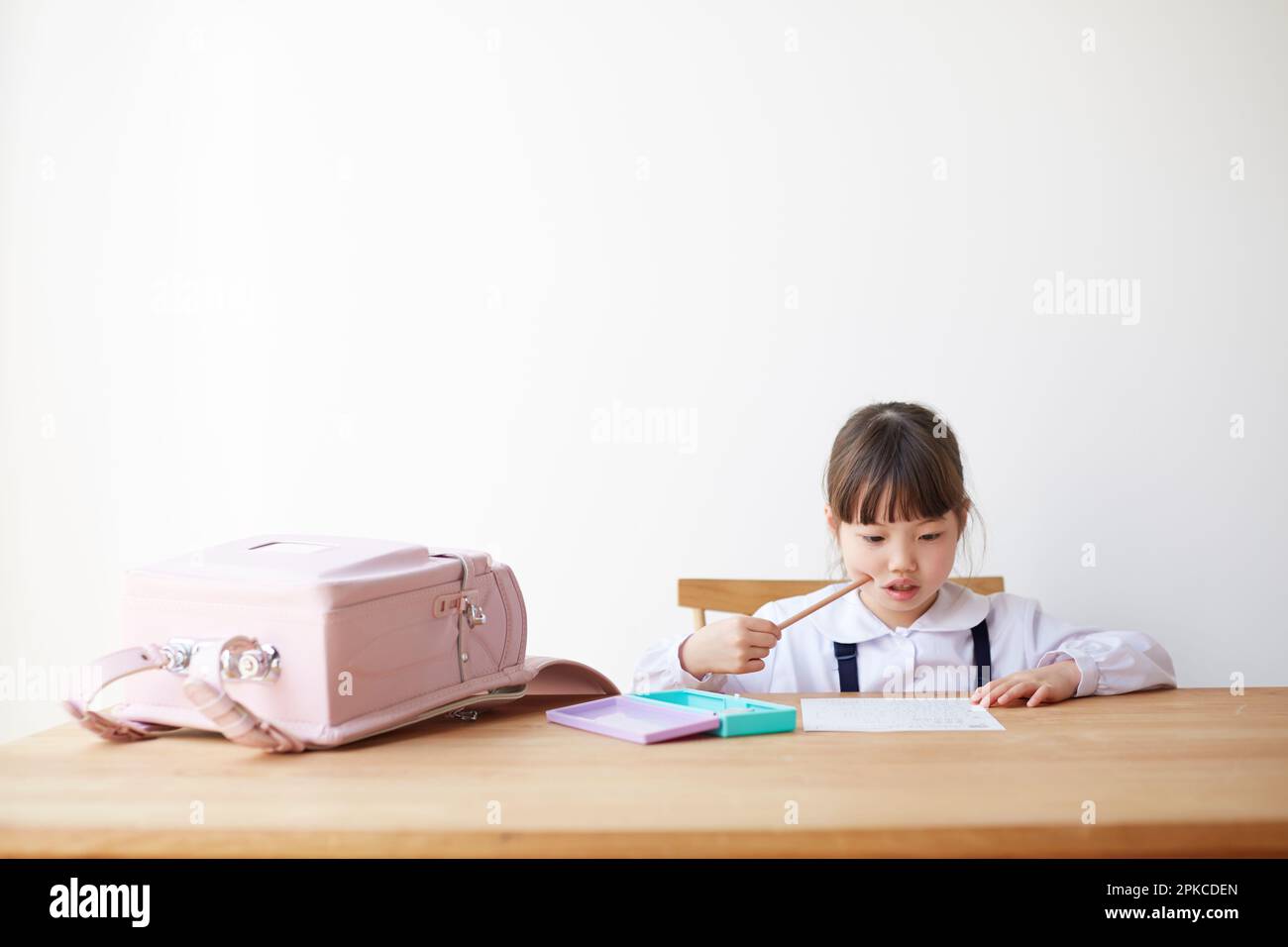 Ragazza che studia con la borsa scolastica sparsa sul tavolo Foto Stock