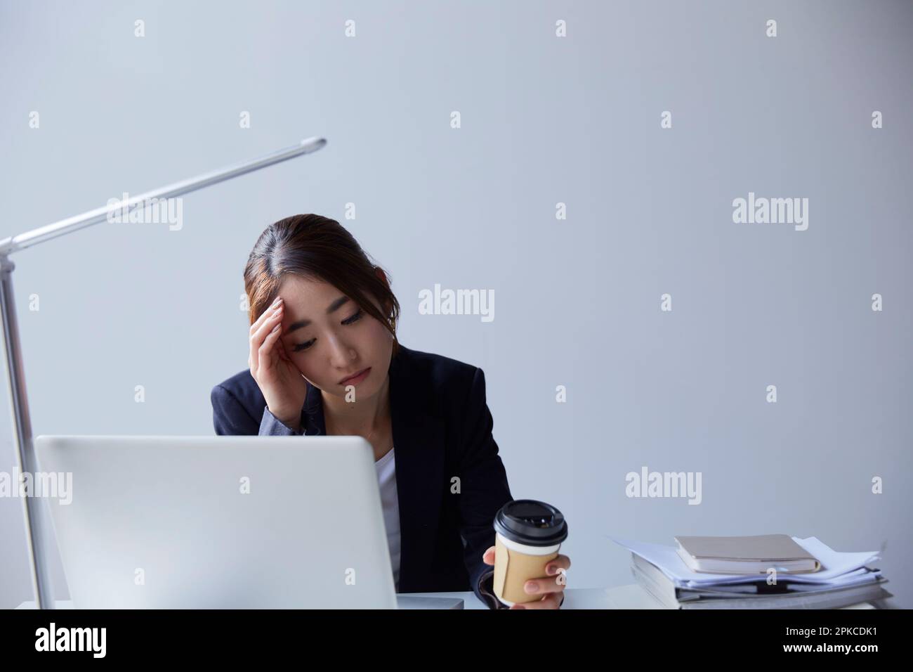 Donna con un'espressione scura sul viso che guarda un computer alla sua scrivania al lavoro Foto Stock