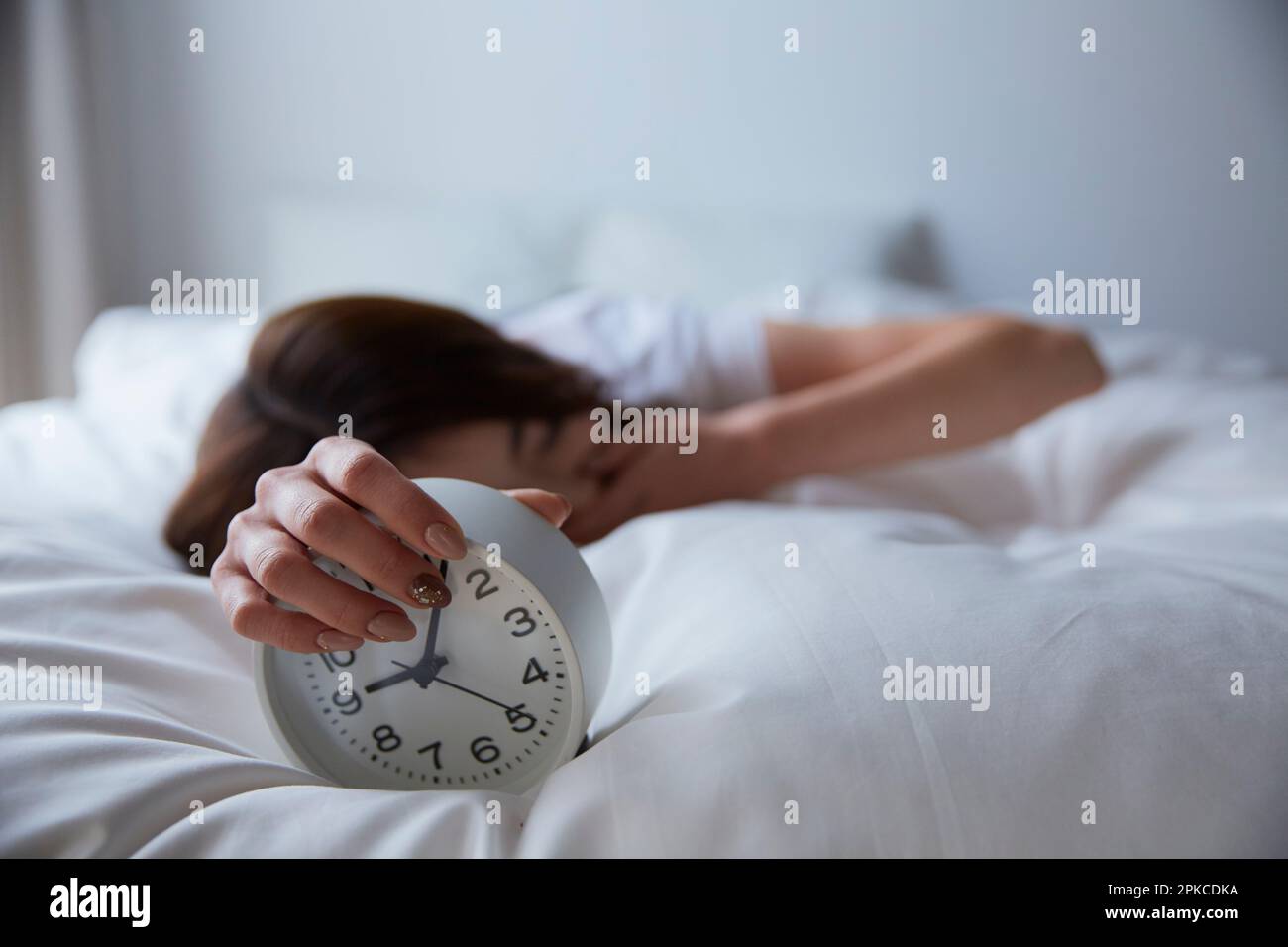 Donna che tiene una sveglia e sbadiglio sul letto Foto Stock