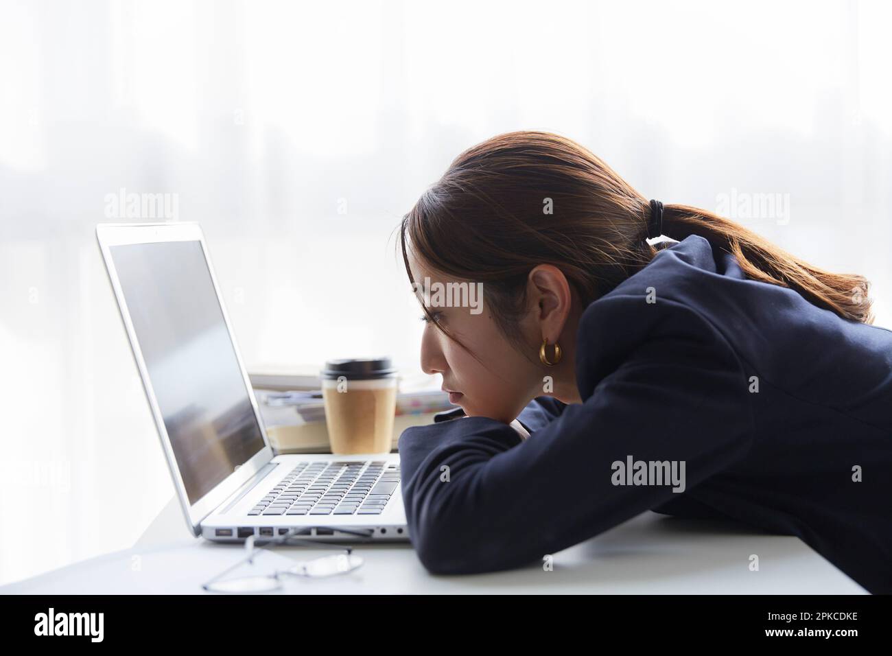 Donna con un'espressione oscura sul viso che guarda il computer alla sua scrivania al lavoro Foto Stock