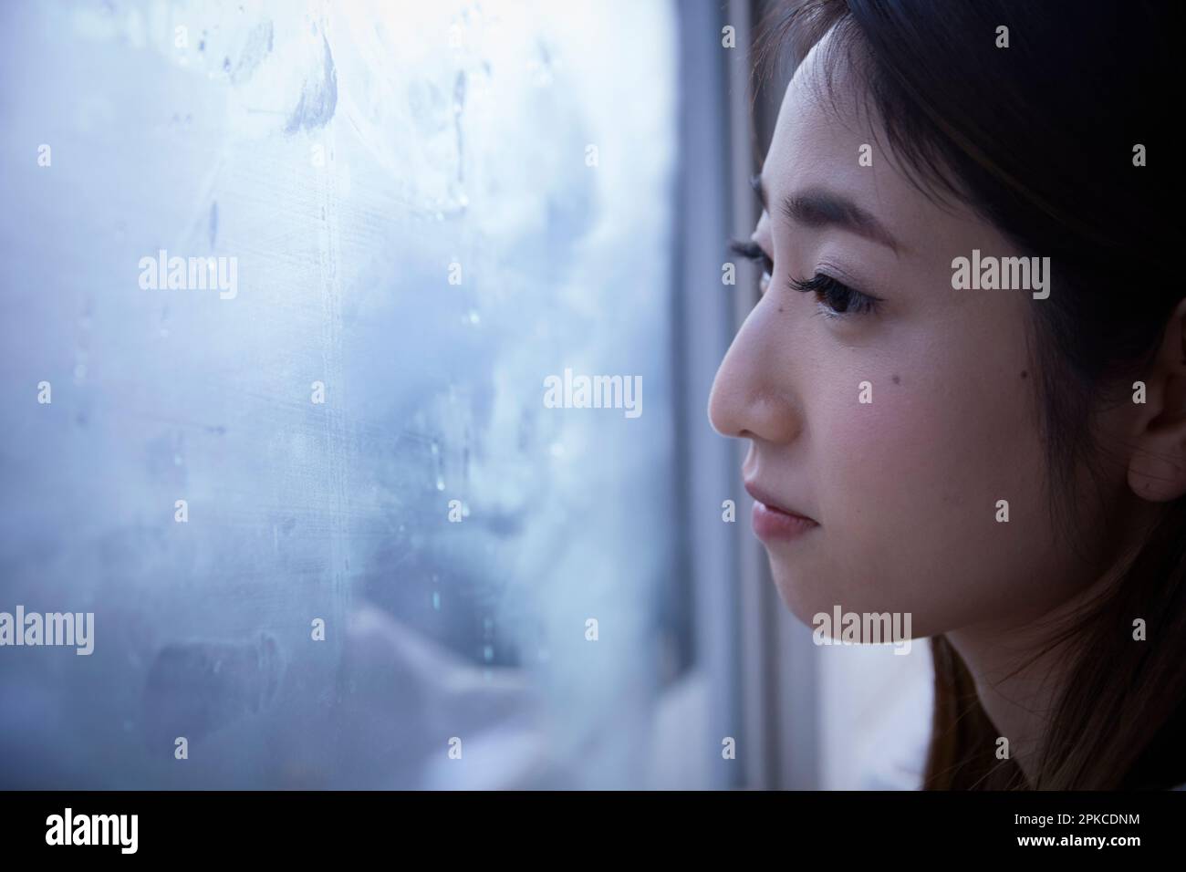 Donna con espressione scura che guarda fuori dalla finestra Foto Stock