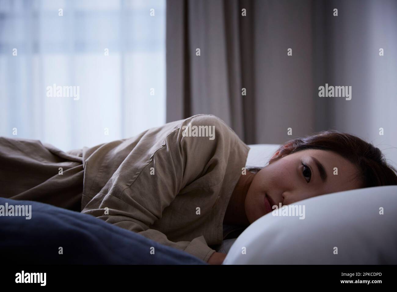 Donna con espressione scura sdraiata sul letto guardando la macchina fotografica Foto Stock