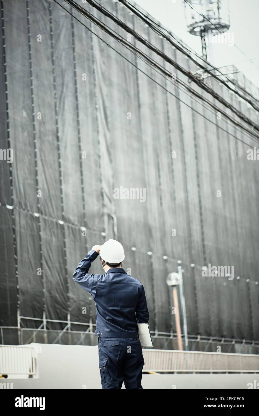 Uomo in abiti da lavoro e casco che guarda l'edificio in costruzione Foto Stock