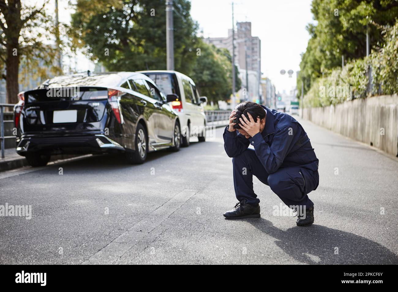 Uomo accovacciato con la testa sulla strada Foto Stock