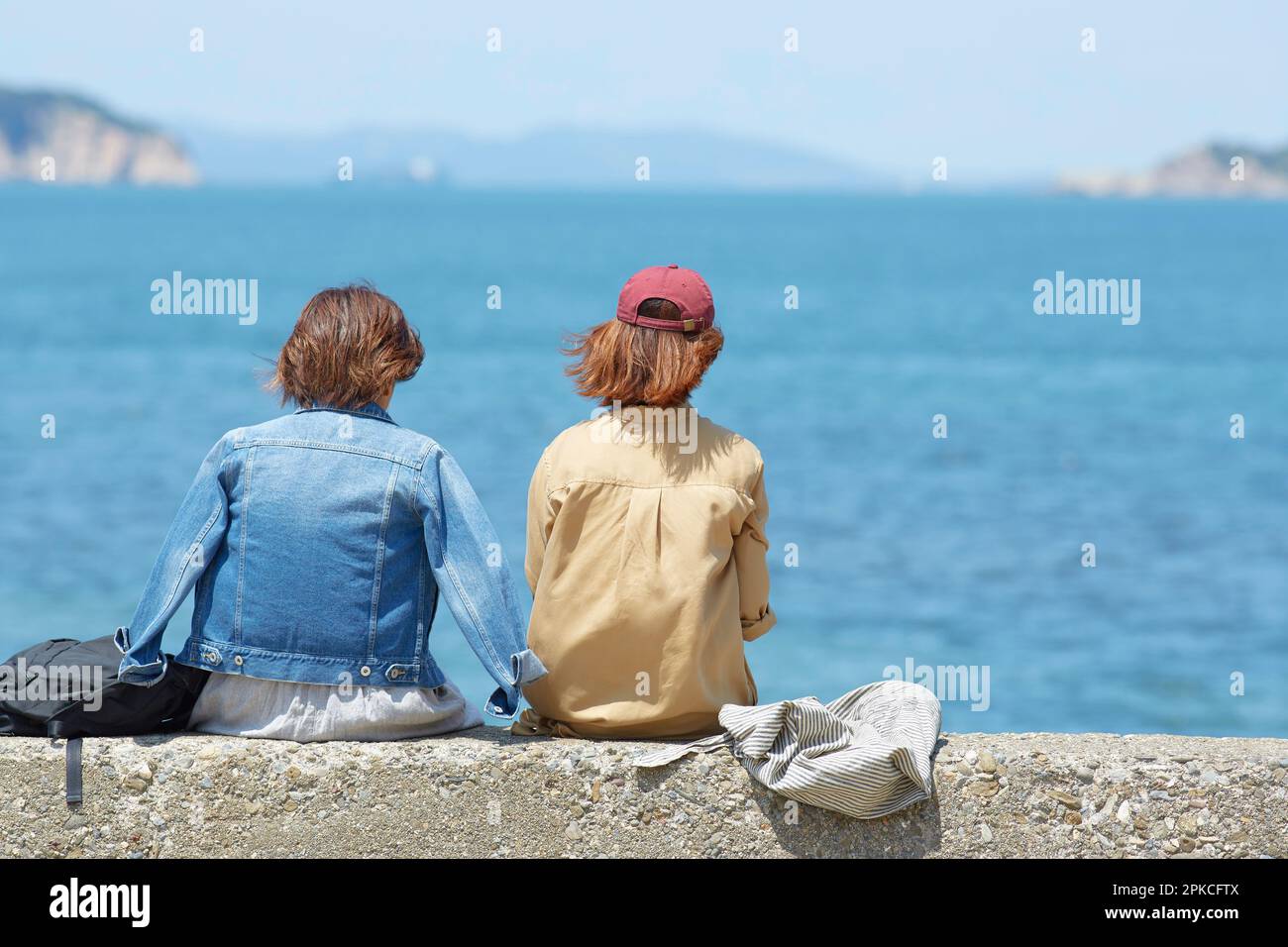 Due donne sedute sul terrapieno che si affacciano sul mare Foto Stock