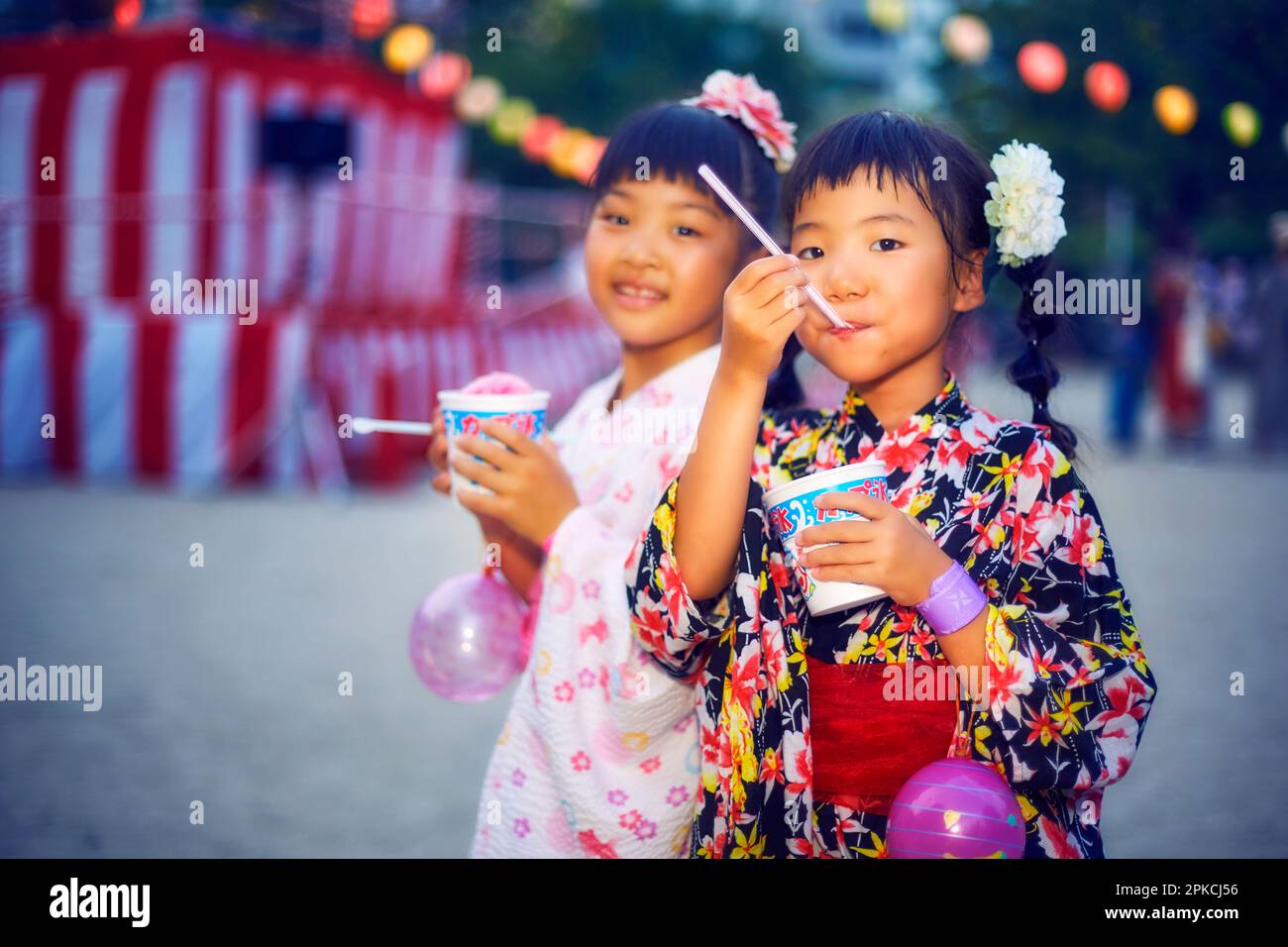 Ragazza in yukata mangiare ghiaccio rasato di fronte a yagura Foto Stock