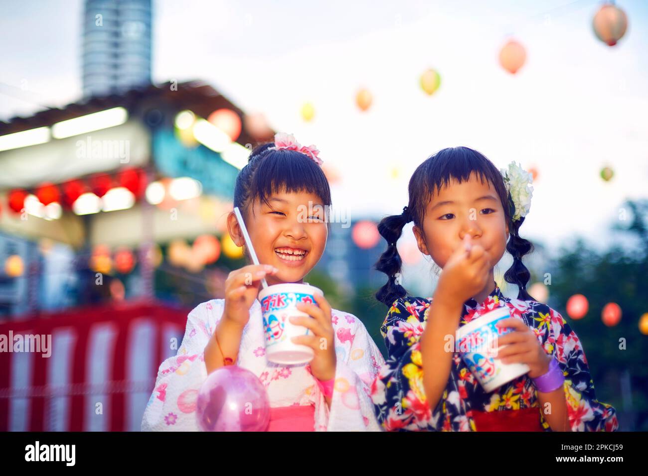 Ragazza in yukata mangiare ghiaccio rasato di fronte a uno stallo Foto Stock