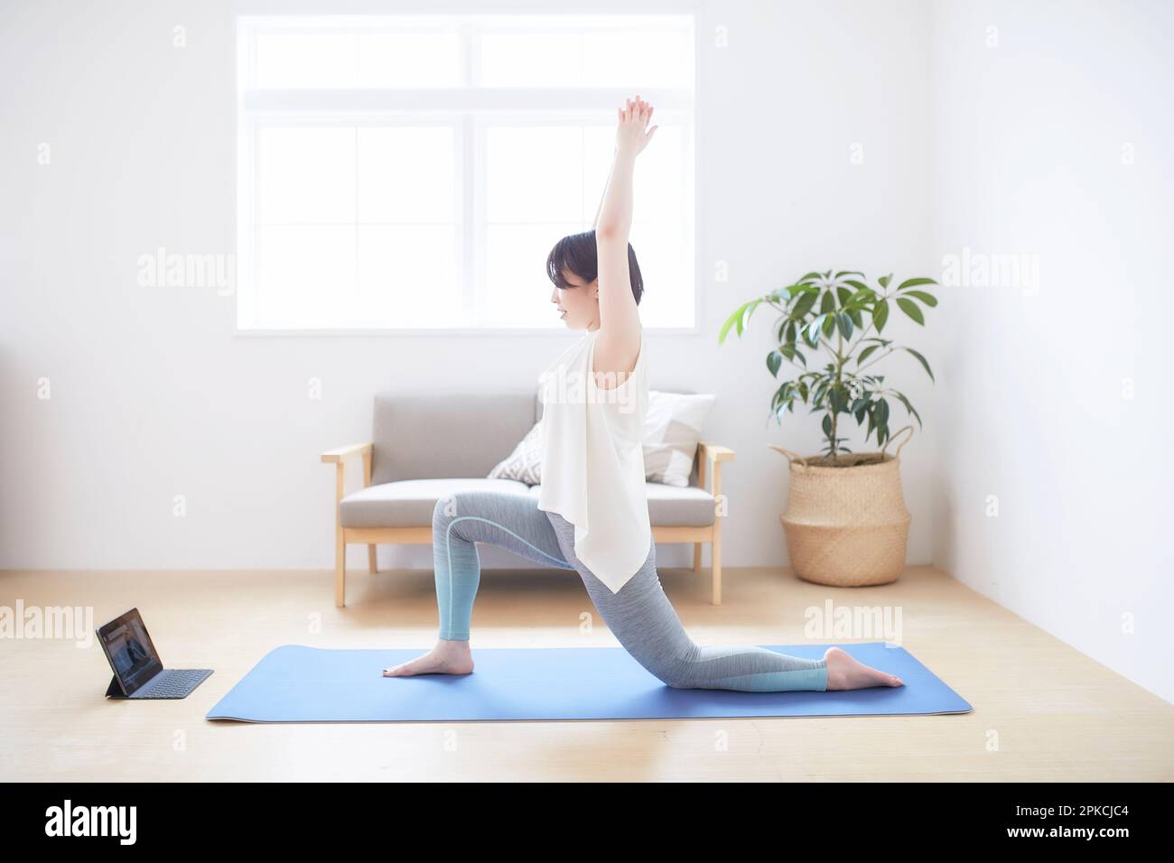 Donna che fa una posa yoga mentre guarda il notebook sul pavimento in casa Foto Stock