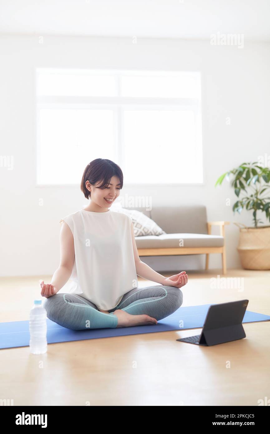 Donna che fa una posa yoga mentre guarda un notebook sul pavimento all'interno Foto Stock