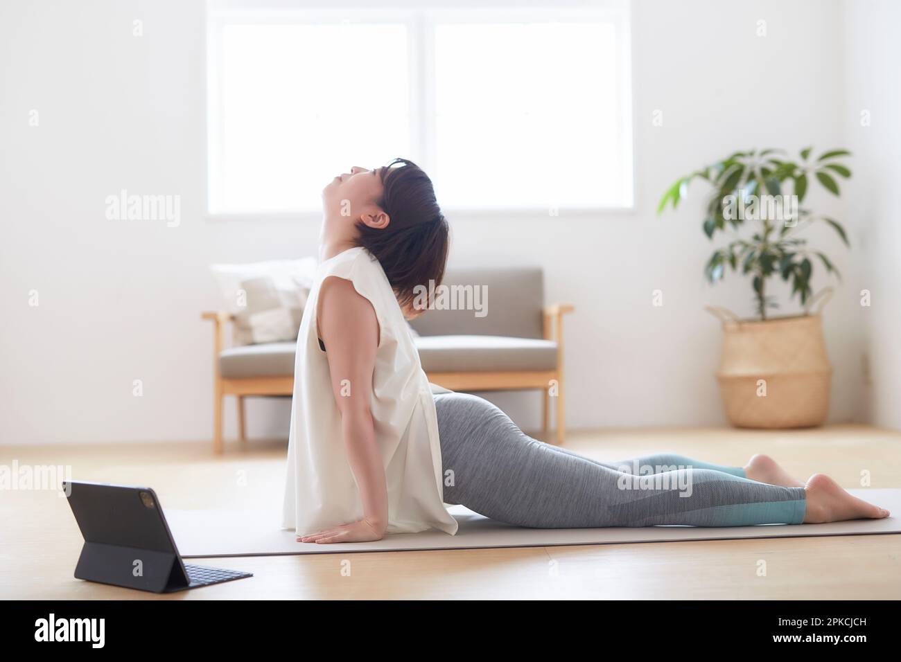 Donna che fa una posa yoga mentre guarda il suo laptop sul pavimento in casa Foto Stock