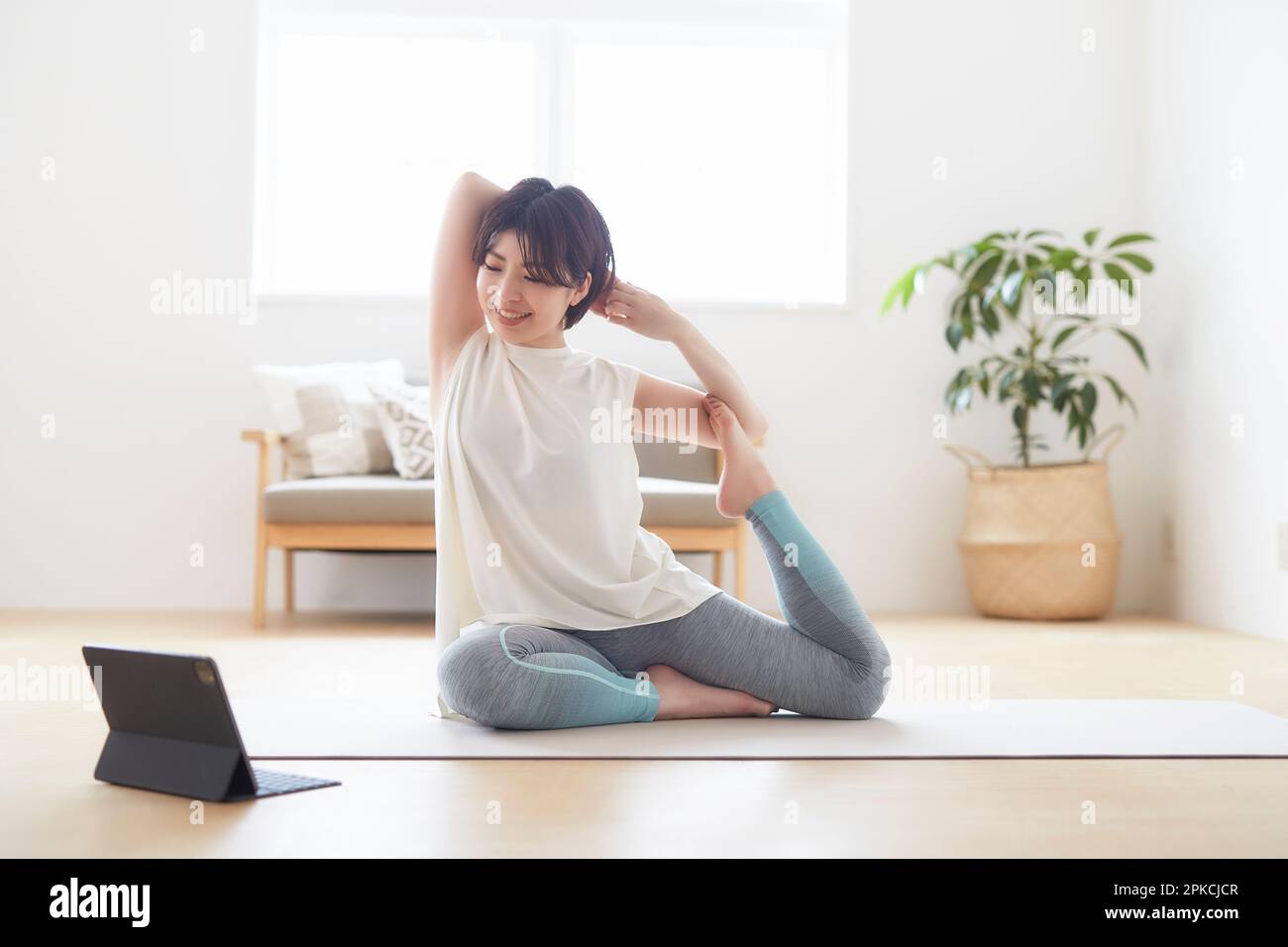 Donna che fa una posa yoga sul pavimento in casa mentre guarda il suo notebook Foto Stock
