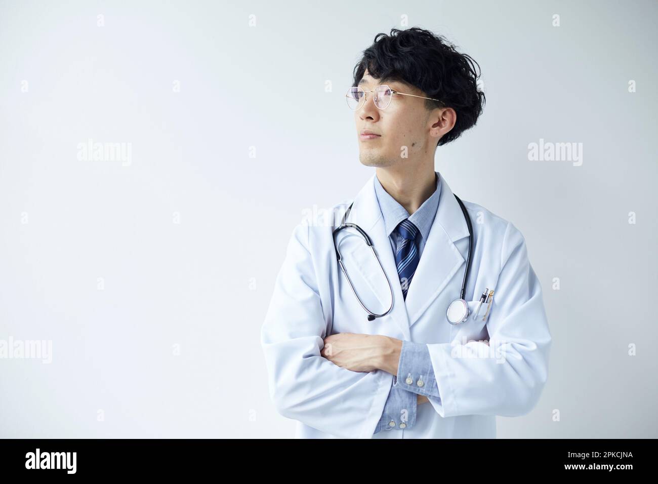 Uomo in bianco in piedi davanti al muro bianco con le braccia incrociate Foto Stock