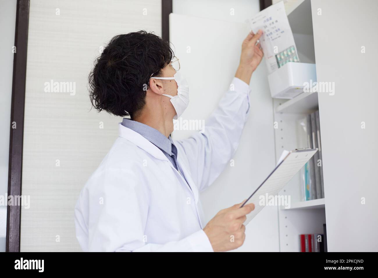 Uomo in bianco che tiene il legante e che prende la medicina dallo scaffale Foto Stock