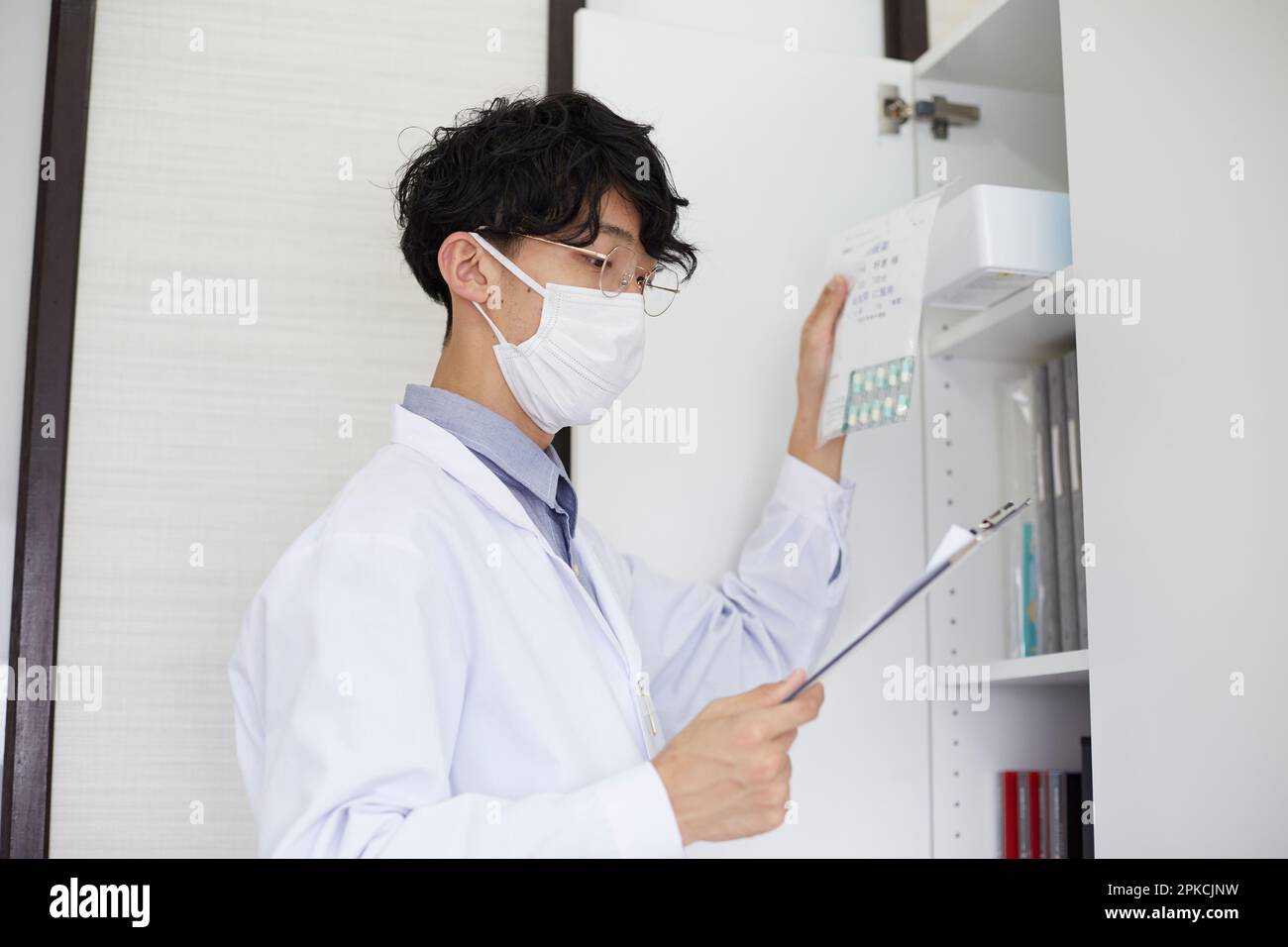 Uomo in bianco che tiene un legante e che prende una medicina da uno scaffale Foto Stock