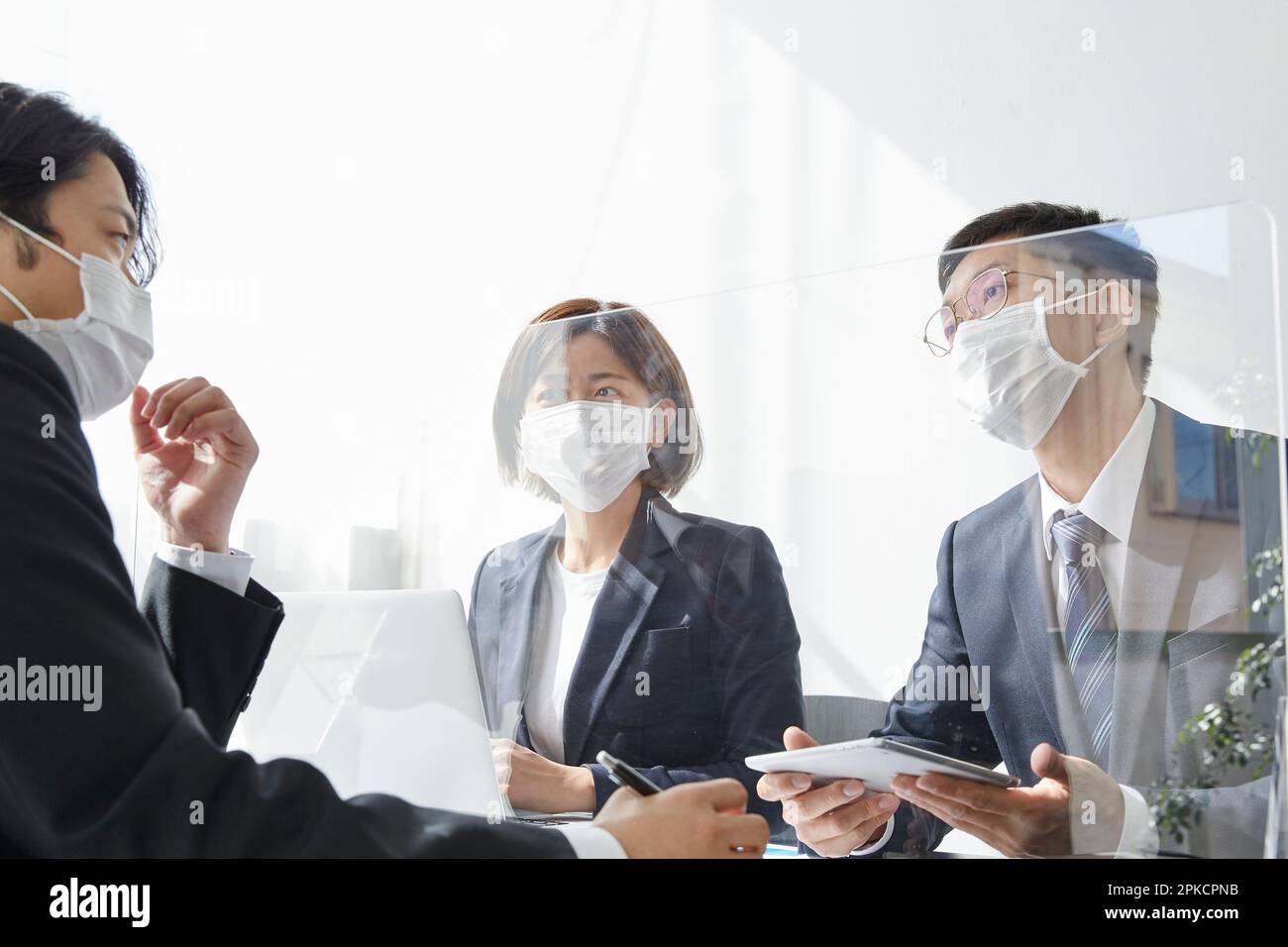 Lavoratore che tiene una riunione aziendale attraverso una partizione con una maschera Foto Stock