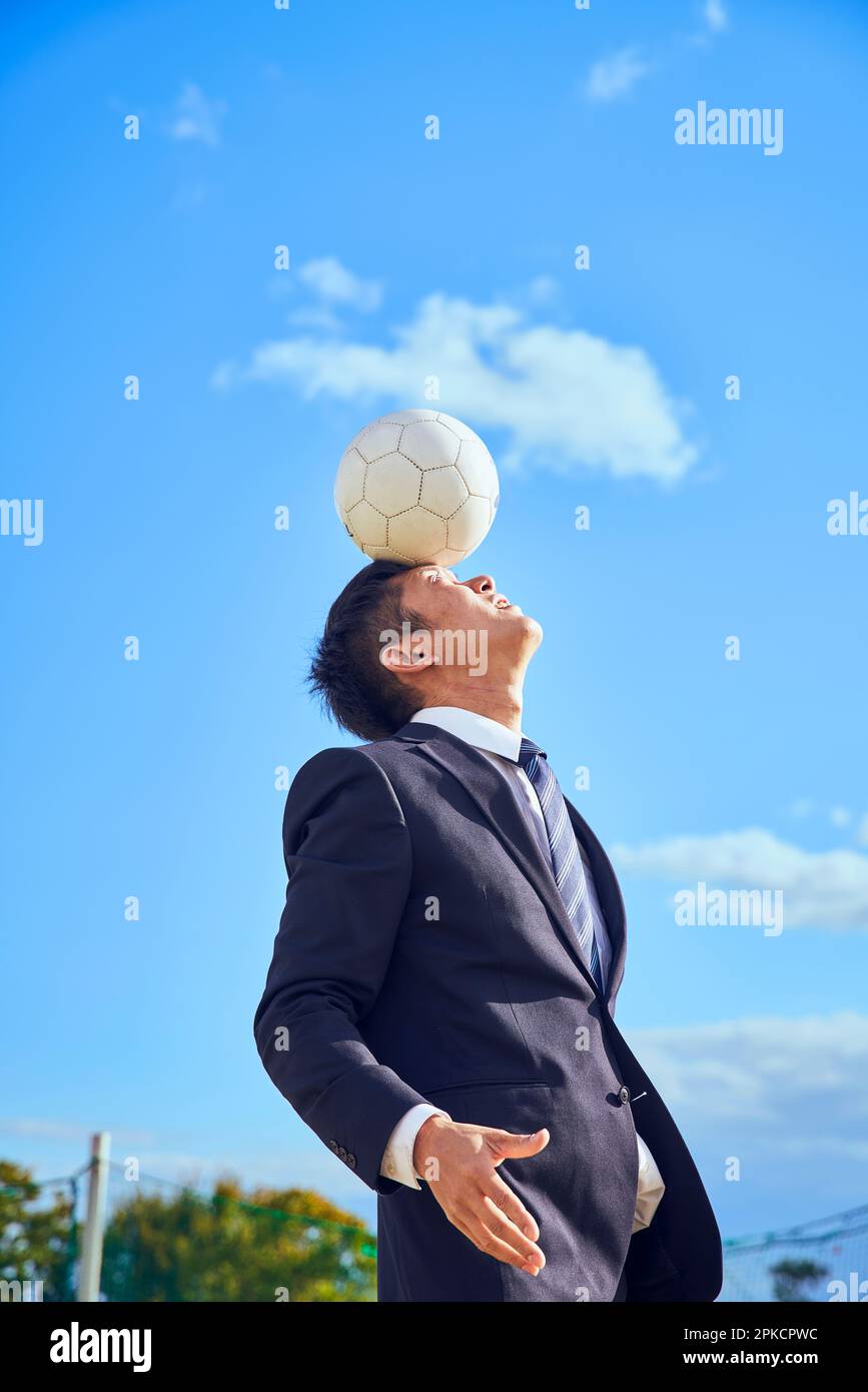 Uomo d'affari che bilancia una sfera sulla sua fronte Foto Stock