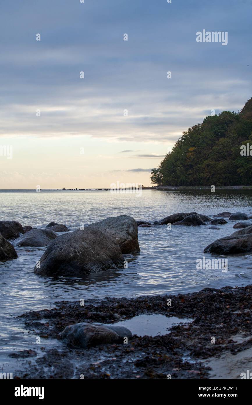Una serena serata sulla costa rocciosa di Rügen, Germania. Massi siedono nel tranquillo Mar Baltico al crepuscolo, creando una scena pacifica e tranquilla. Foto Stock