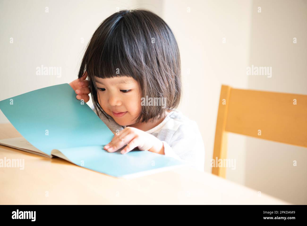 Ragazza che apre un libro di immagini al tavolo Foto Stock