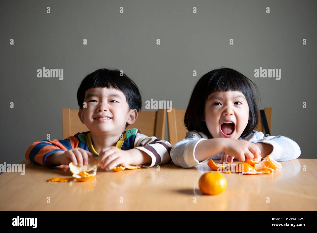 I bambini ridono mentre si pelano i tangerini Foto Stock