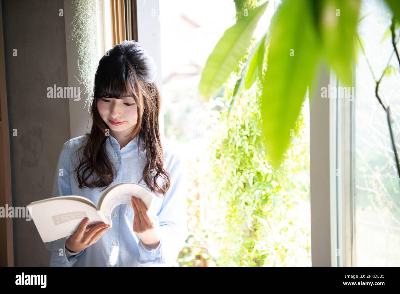 Donna che legge un libro dalla finestra Foto Stock