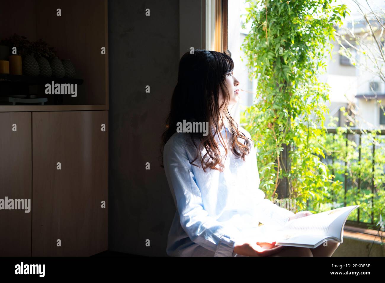 Donna seduta sul libro di lettura del windowsill Foto Stock
