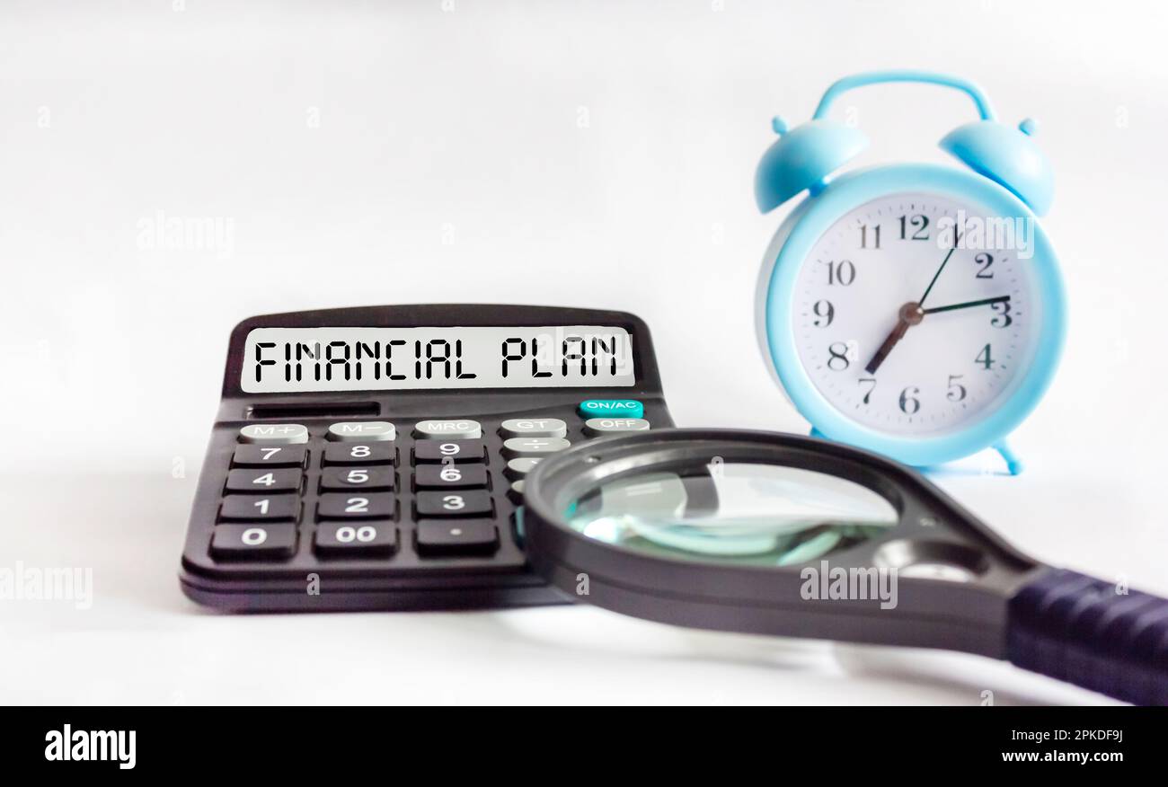 Calcolatrice con il testo DEL PIANO FINANZIARIO su sfondo bianco, accanto ad esso è una lente d'ingrandimento. Concetto finanziario. Foto Stock