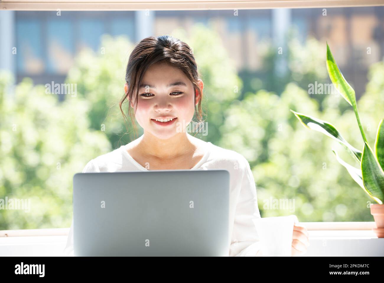 Donna che utilizza un computer con una tazza di tè in mano dalla finestra Foto Stock