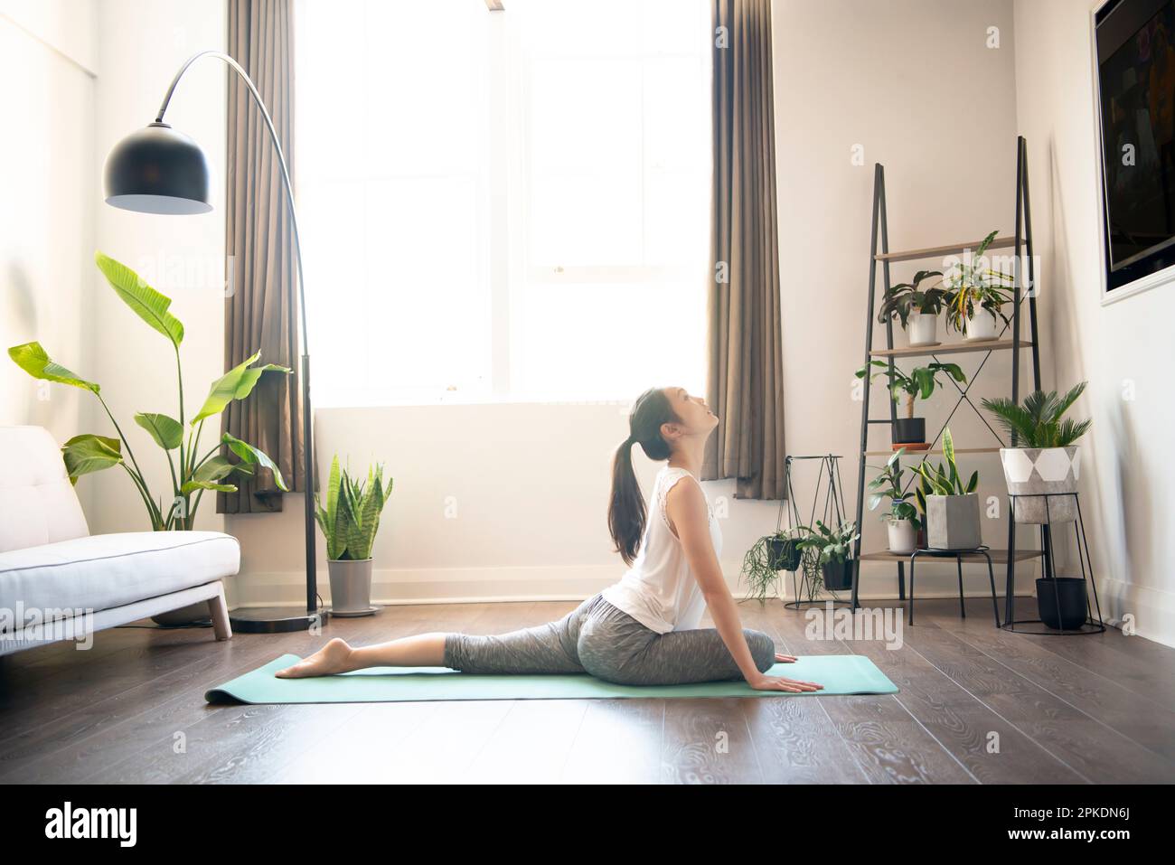 Donna che fa yoga nel soggiorno di casa sua Foto Stock