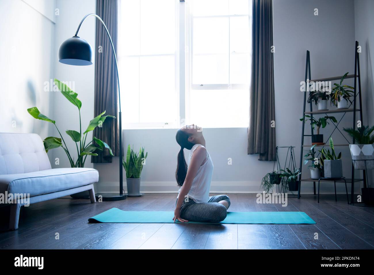 Donna che fa yoga nel suo salotto Foto Stock