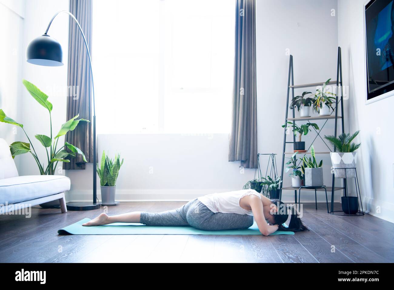 Donna che fa yoga nel soggiorno di casa sua Foto Stock