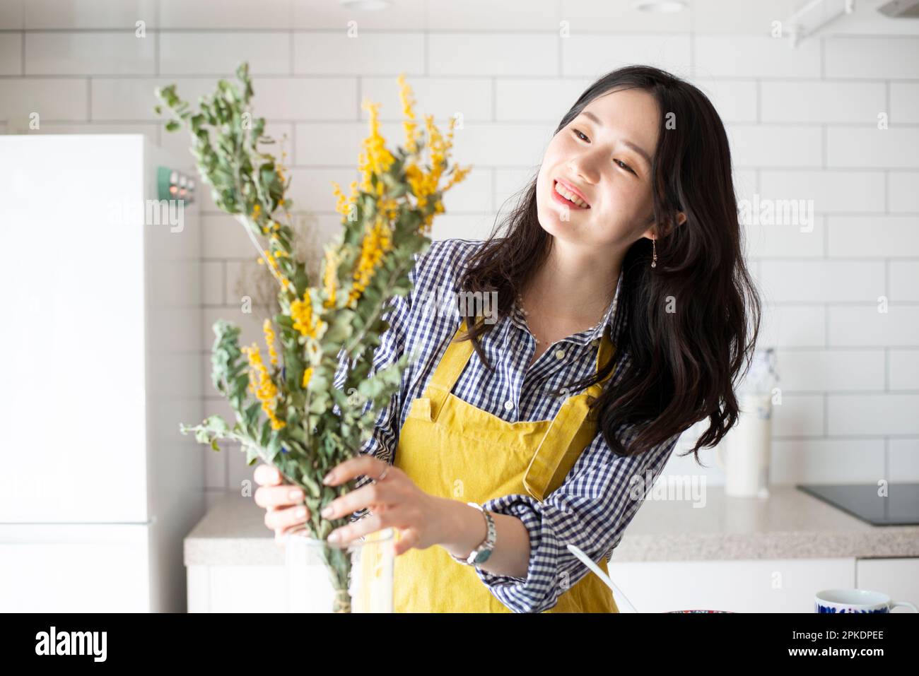 Donna con grembiule che mostra fiori in cucina Foto Stock