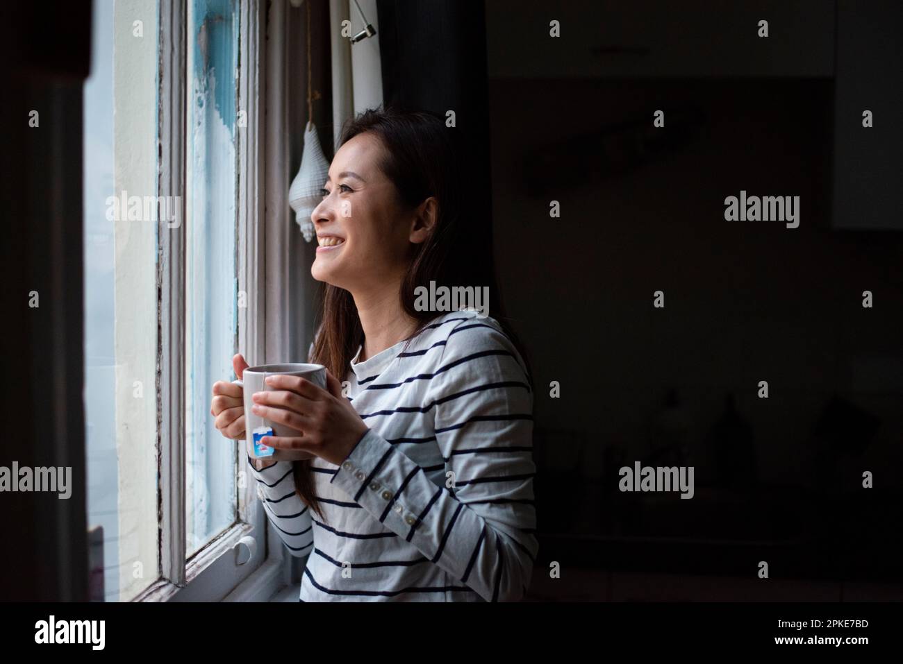 Donna con una bevanda calda alla finestra Foto Stock