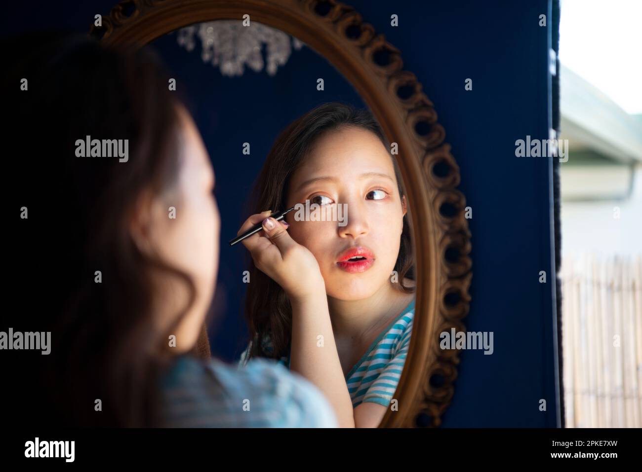 Donna che fa il trucco dell'occhio mentre osserva nello specchio Foto Stock