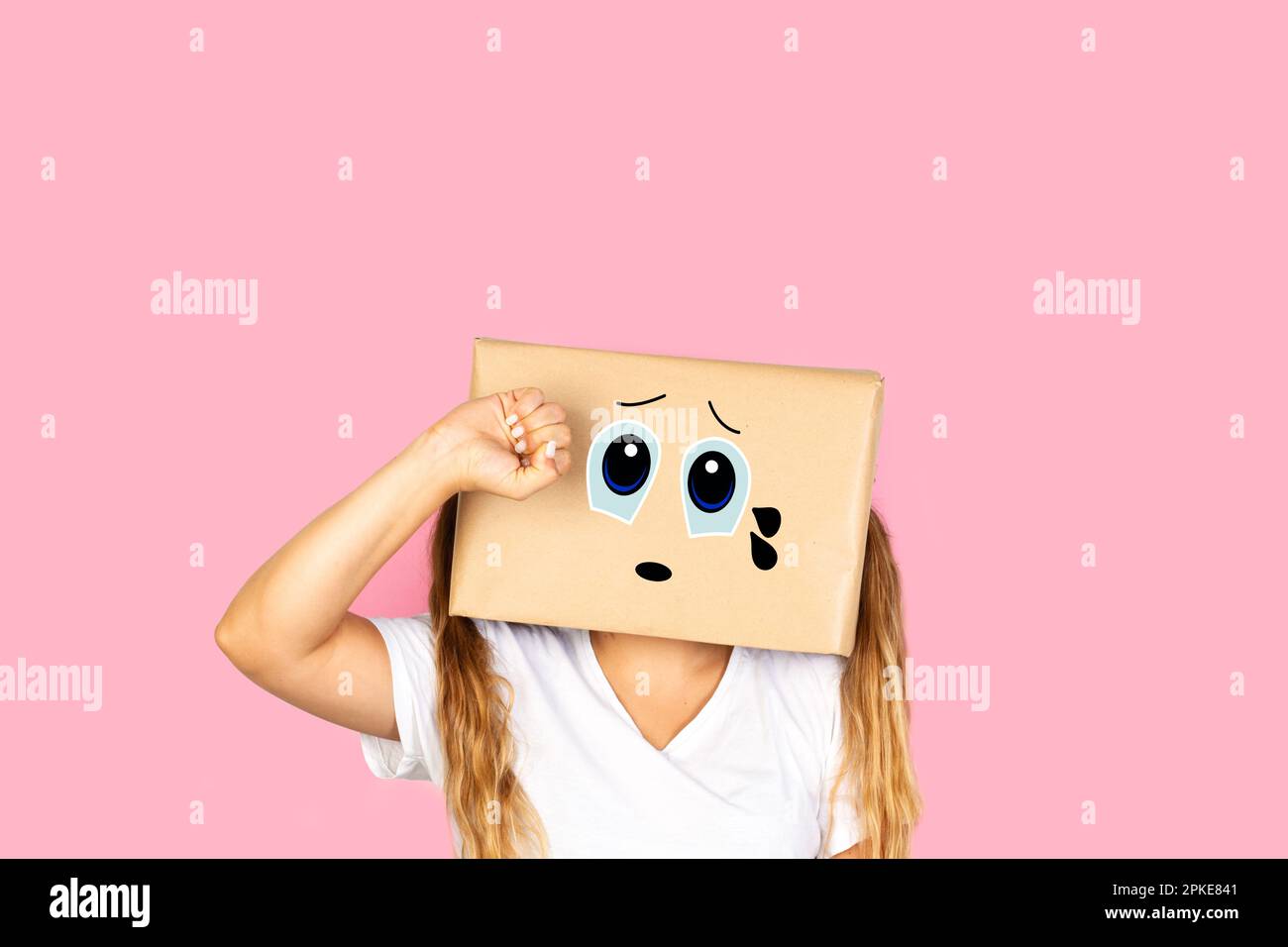 Donna con la testa in una scatola e gesto piangente in piedi su uno sfondo rosa con spazio copia Foto Stock