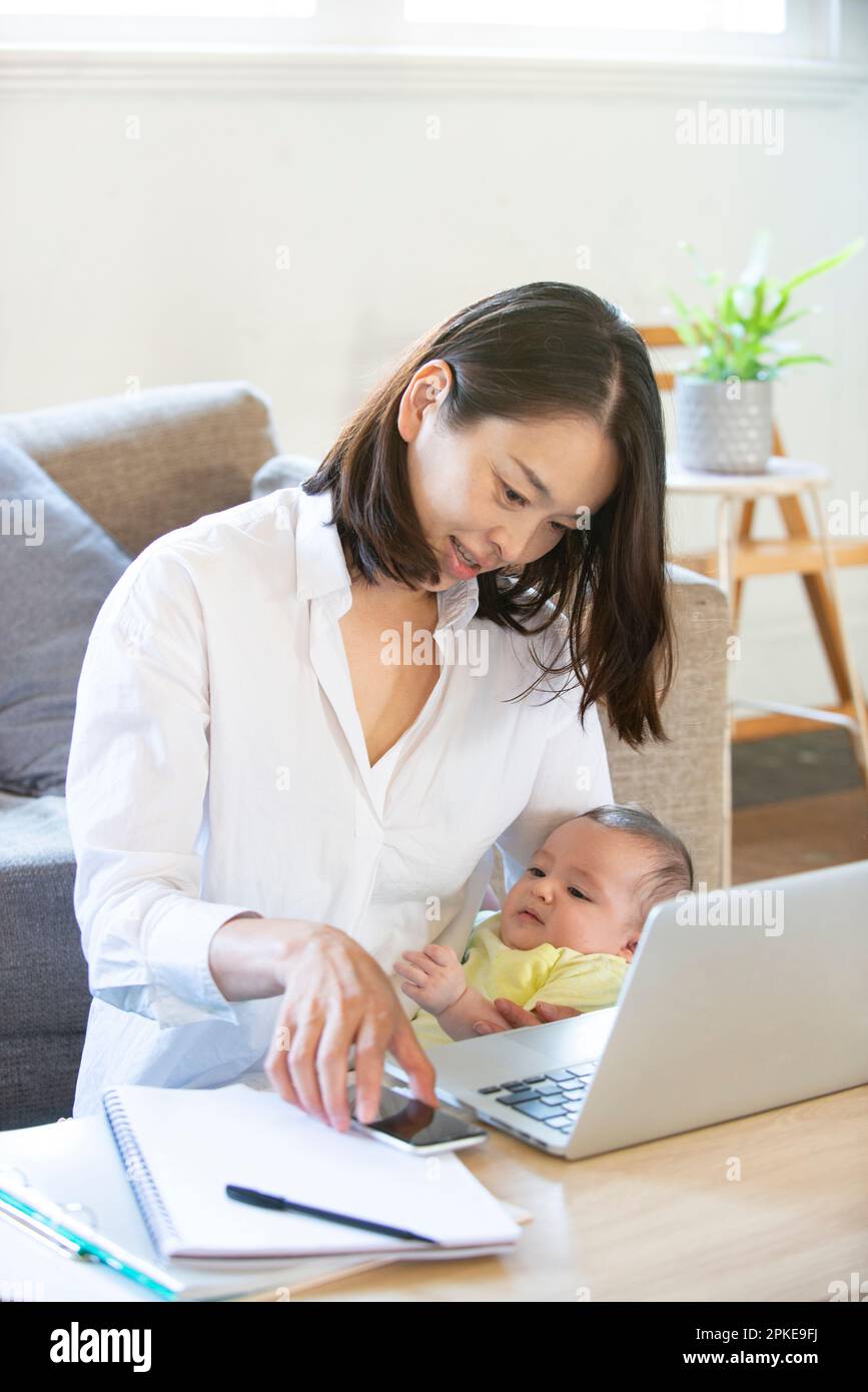 Donna che lavora a casa con il bambino in braccio Foto Stock