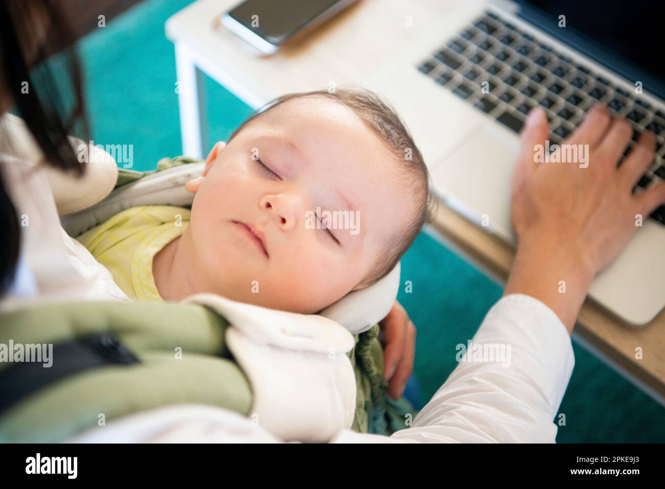Donna che lavora al computer con il bambino in braccio Foto Stock