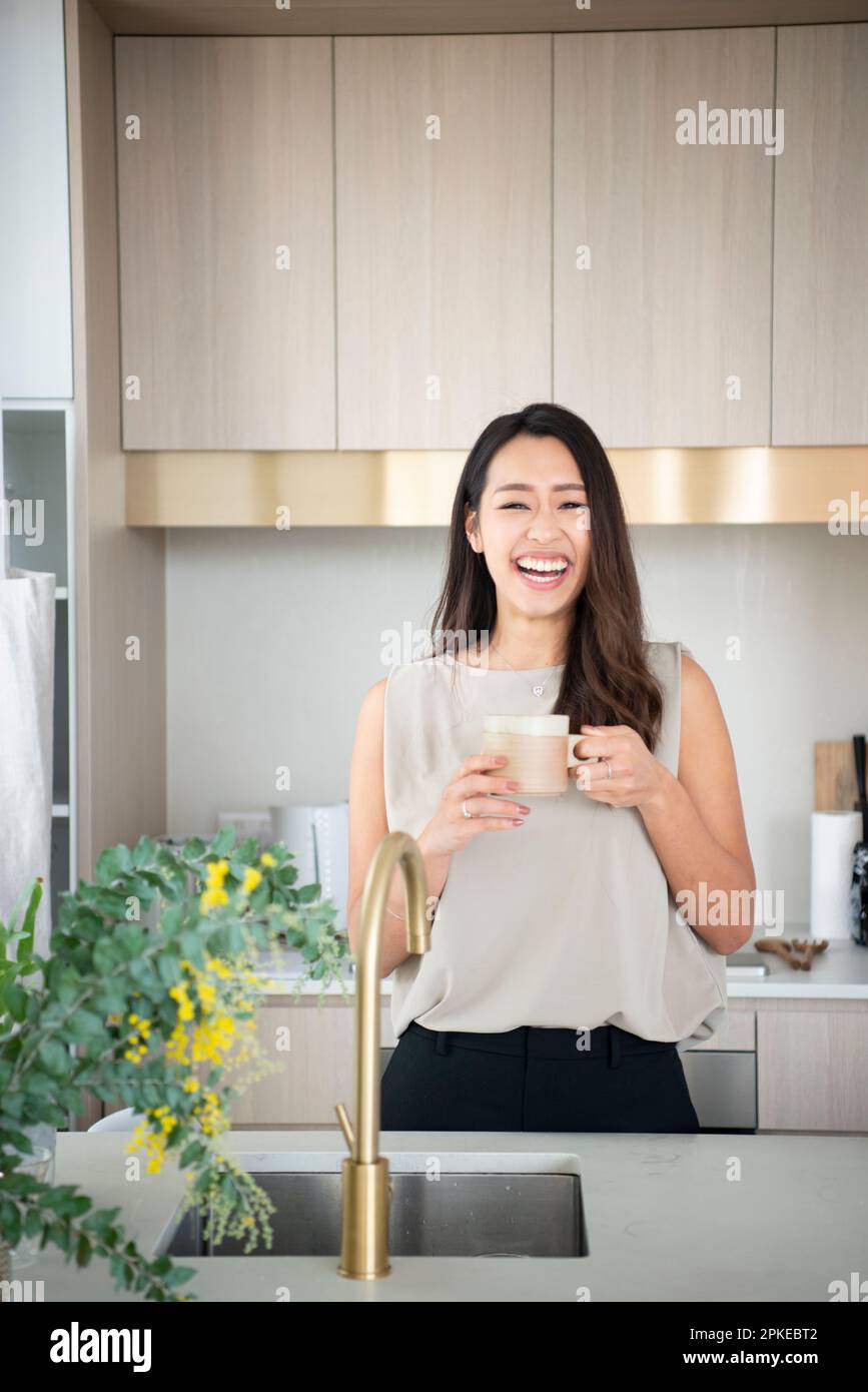 Donna che ride con la tazza in cucina Foto Stock
