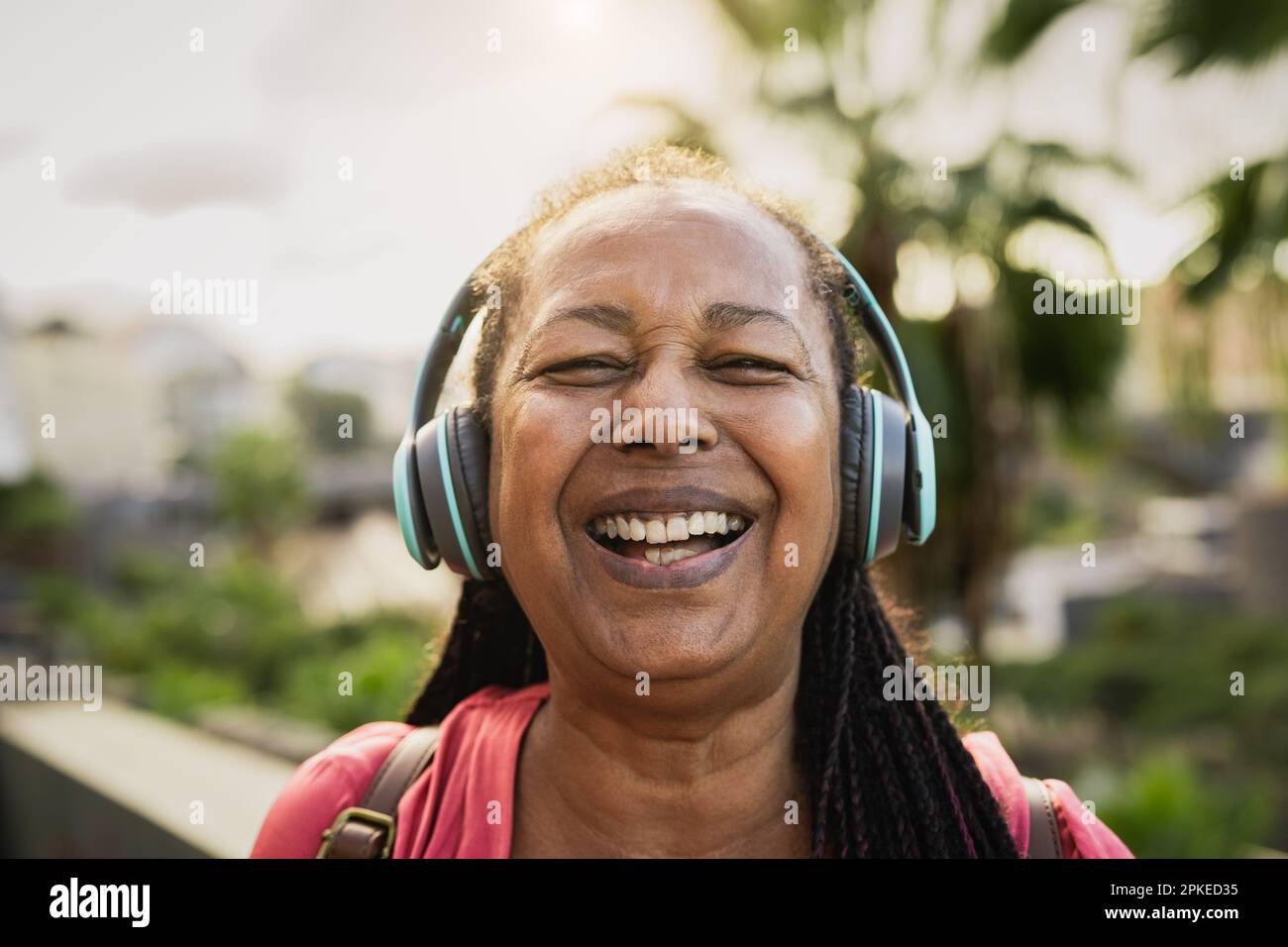 Felice donna africana anziana che ascolta musica con cuffie wireless mentre sorride nella fotocamera Foto Stock