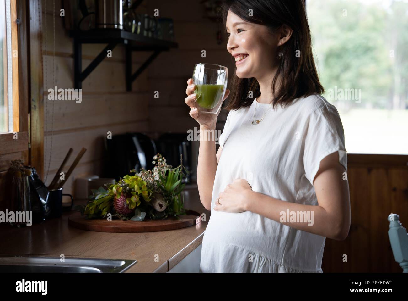 Donna incinta che tiene un bicchiere di bevanda in cucina Foto Stock