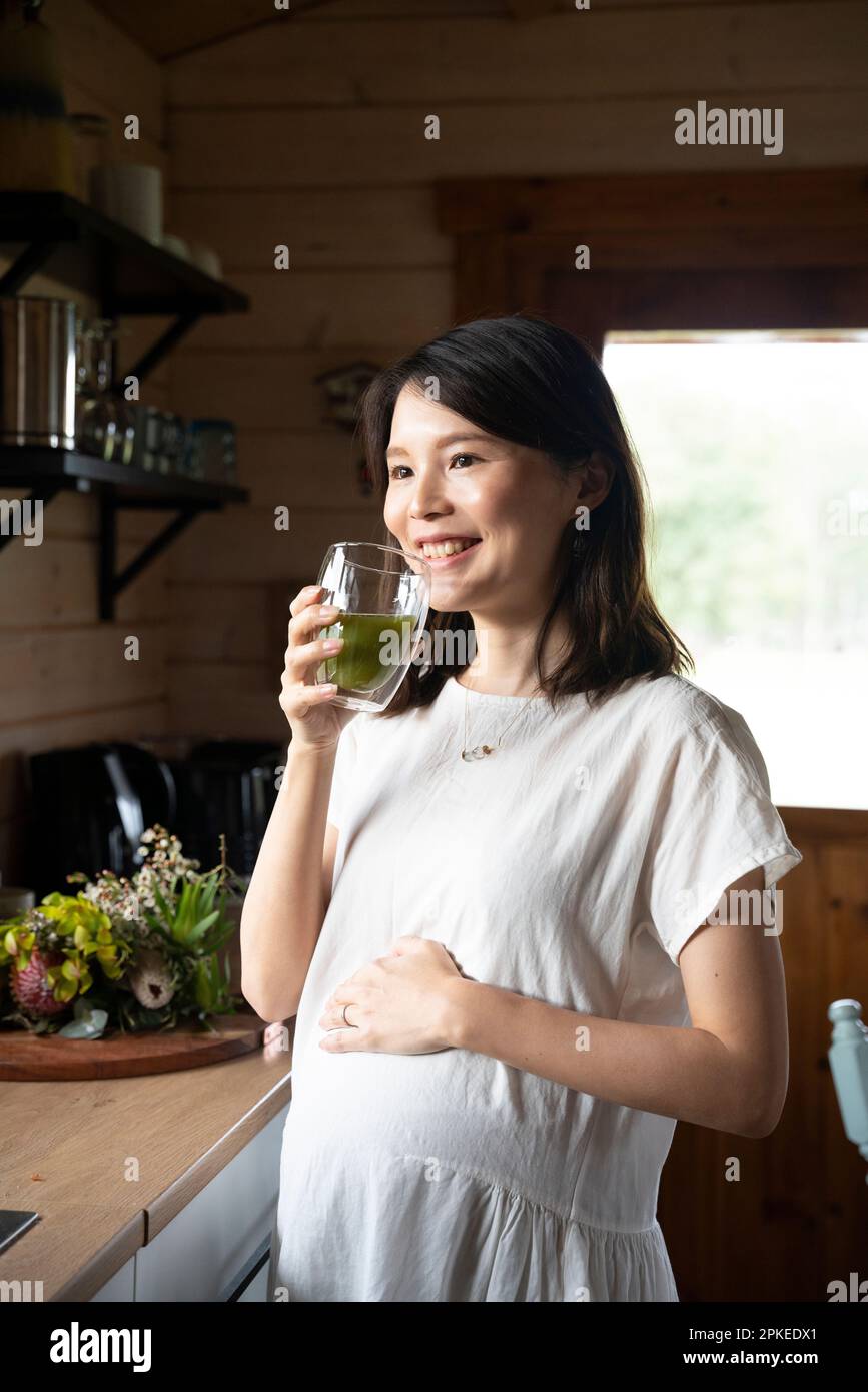 Donna incinta che tiene un bicchiere di bevanda in cucina Foto Stock