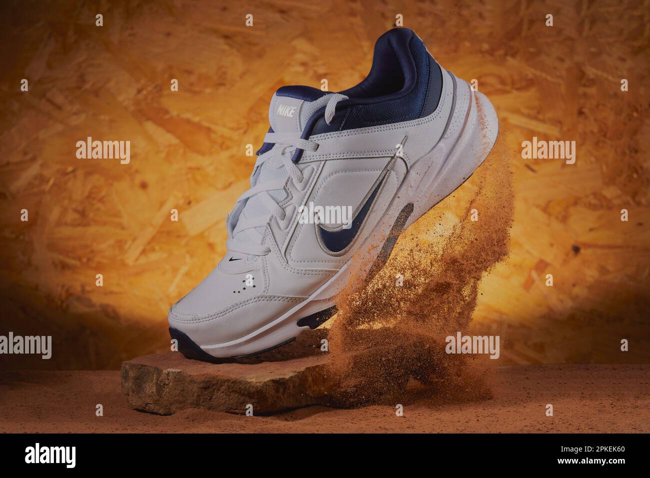 Foto da studio di un paio di scarpe da ginnastica Nike appoggiate su una pietra con sabbia che viene calciata dietro di loro. Foto Stock
