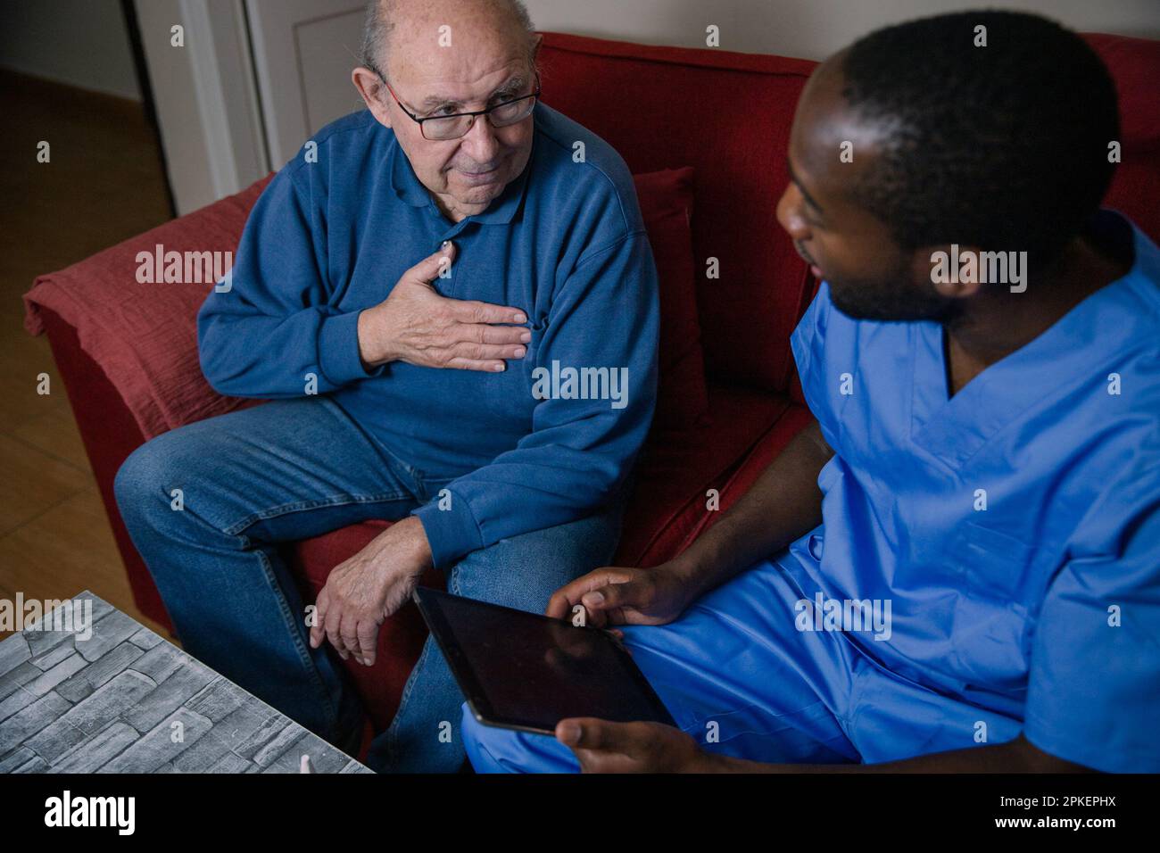 Un medico afro-americano che parla con il suo paziente anziano il cui petto fa male. Foto Stock