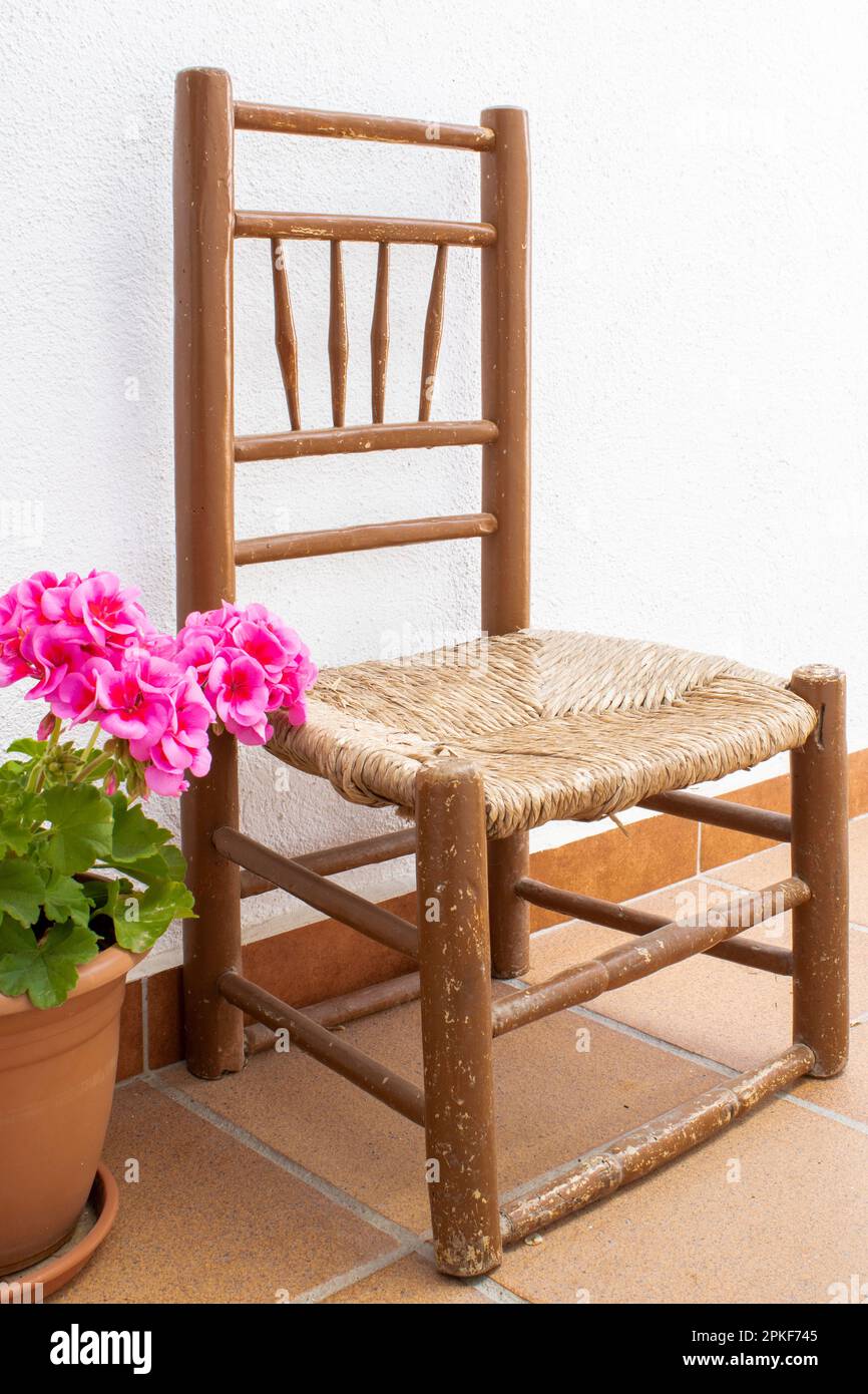 Piccola sedia antica con geranio rosa con sfondo bianco parete. Foto Stock