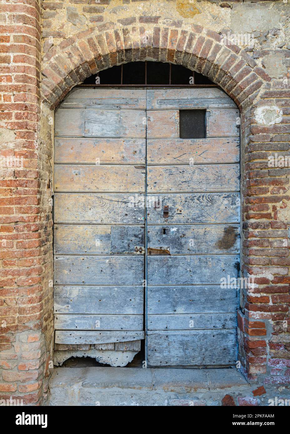 Arco in mattoni con fatiscenti porte blu e verdi in Toscana Foto Stock